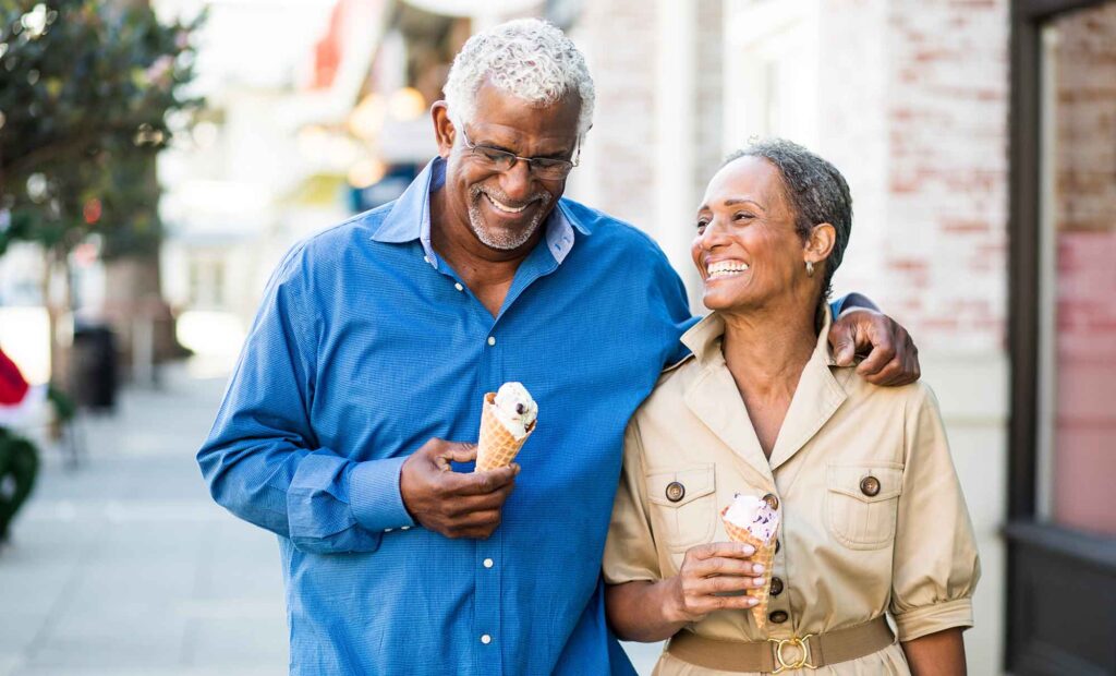 Senior couple walk down a city street with ice cream and laughing